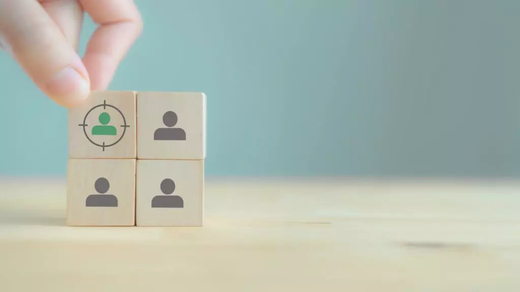 Produtos Atemporais: Como Montar um Pedido Inteligente e Lucrar Rápido 2 Blocos de madeira com ícones de pessoas representando a definição de público-alvo.