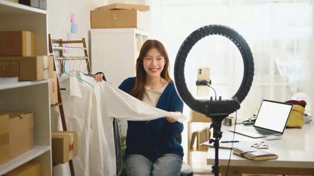 Produtos Atemporais: Como Montar um Pedido Inteligente e Lucrar Rápido 3 Mulher com cabelos longos e escuro, representando uma criadora de conteúdo, apresentando roupas em vídeo com ring light.