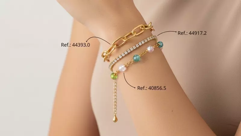 Mulher usando mix de pulseiras douradas, incluindo corrente de elos, pulseira com pedras coloridas e modelo com zircônias, criando composição moderna e delicada no pulso.